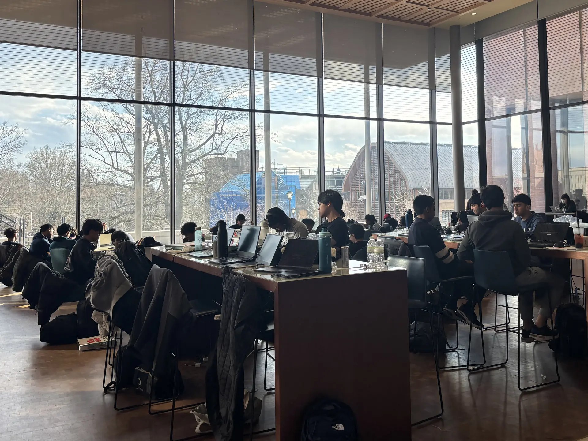Students working in groups at tables beside large windows